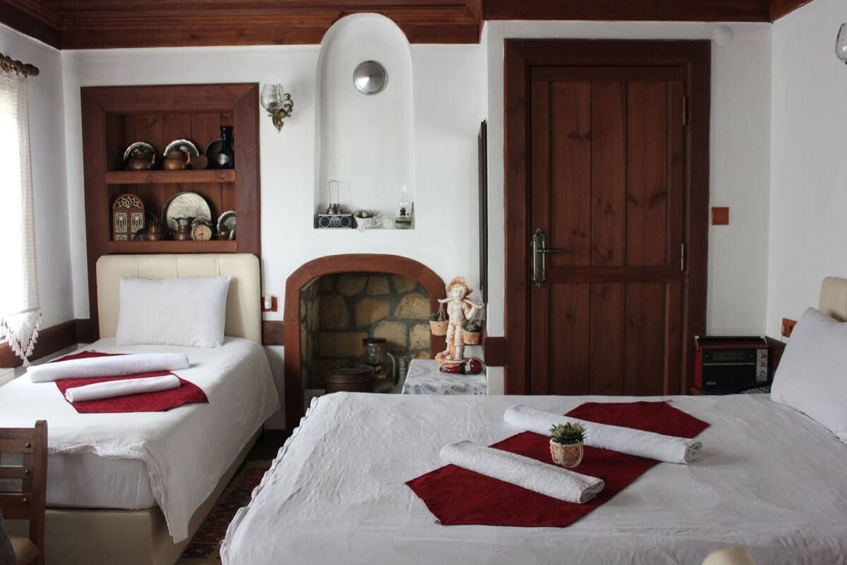 A hotel room with two beds, a fireplace, a wooden door, and a shelf with decorative items.