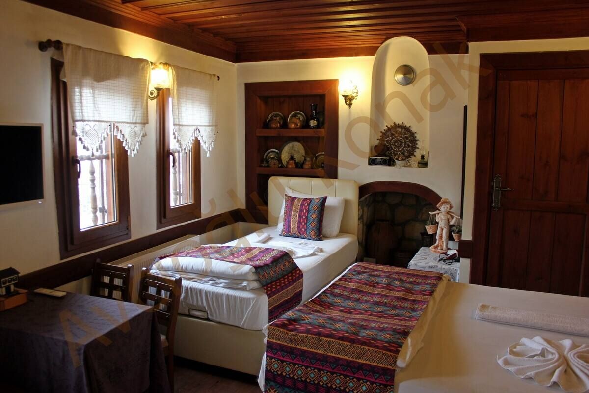 Quarto com duas camas de solteiro, uma mesa de madeira, lareira e uma estante com objetos decorativos.