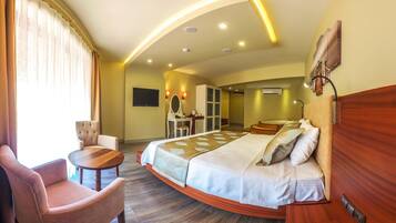 A hotel room with a curved bed, a sitting area with a table and chairs, a TV, and a bathroom with a shower and toilet.