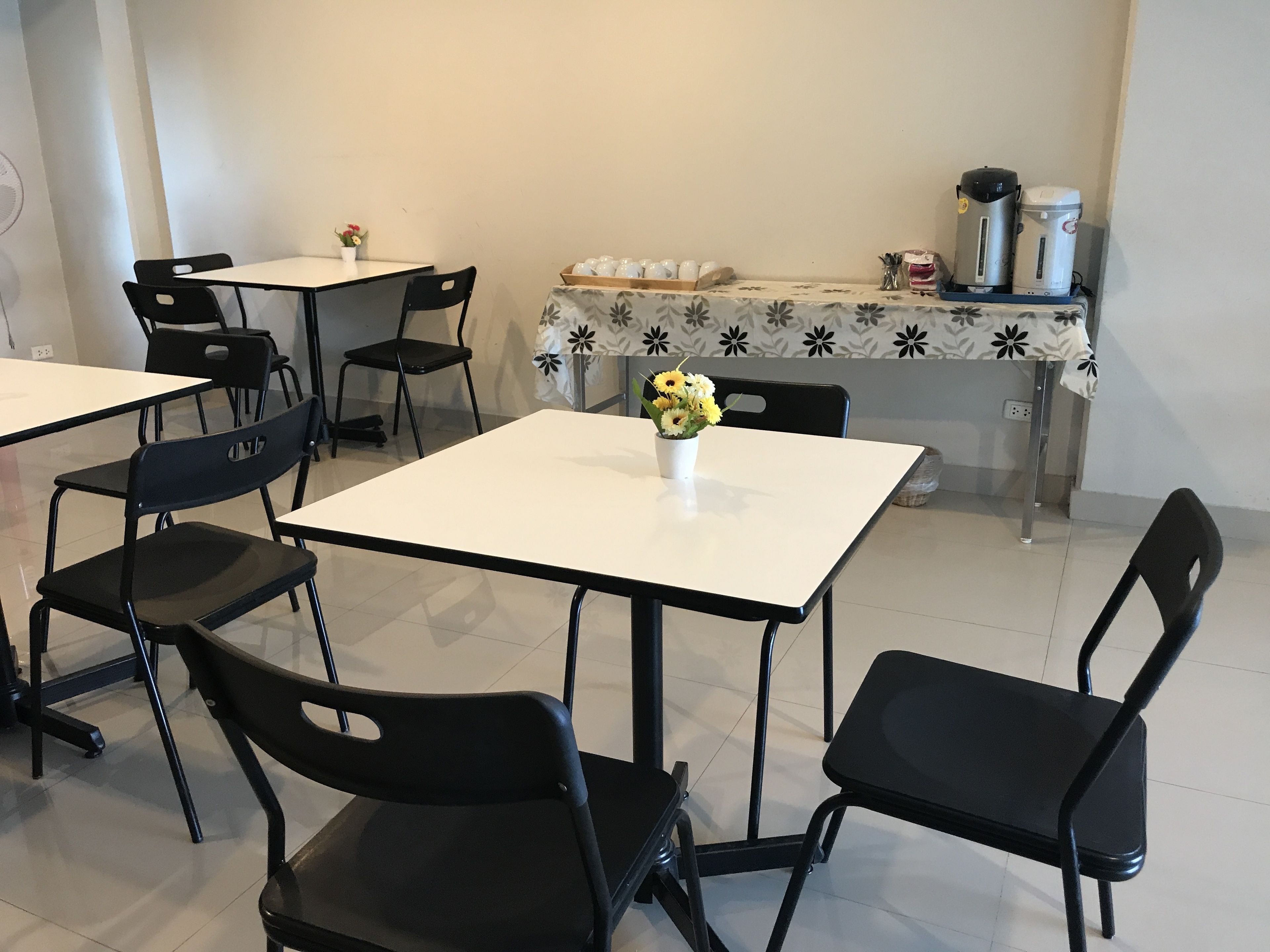 A dining area with tables and chairs, a flower vase, and a table with a floral tablecloth.