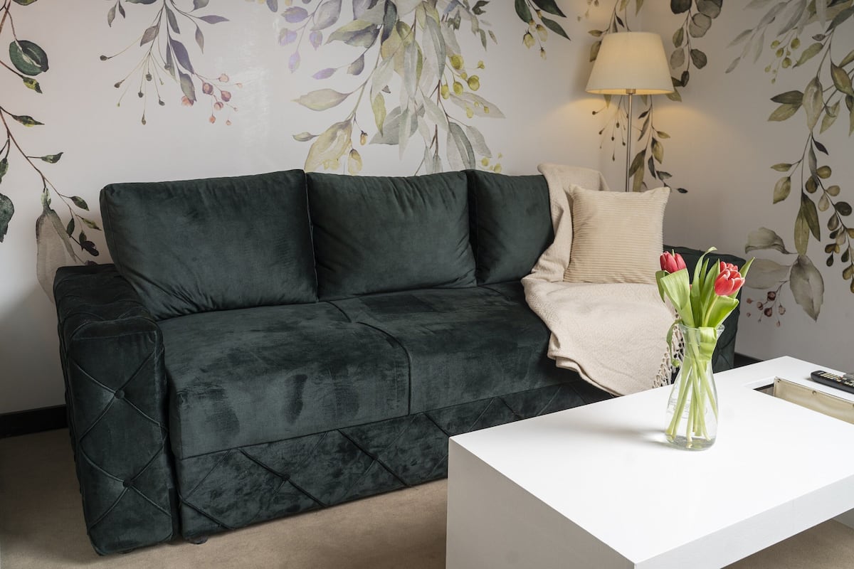 A dark green sofa with a white side table and a vase with red flowers.