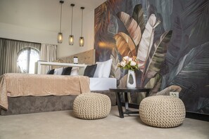 A modern bedroom with a bed, two woven poufs, a small table, and a large leaf-patterned wall. - Villa Akacija (Belgrade)