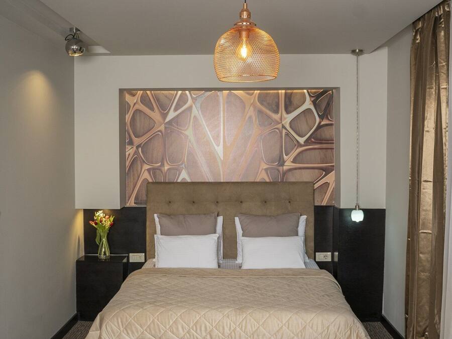 Habitación de hotel con una cama grande, cabecera de madera, lámpara de techo redonda y pared con diseño abstracto.
