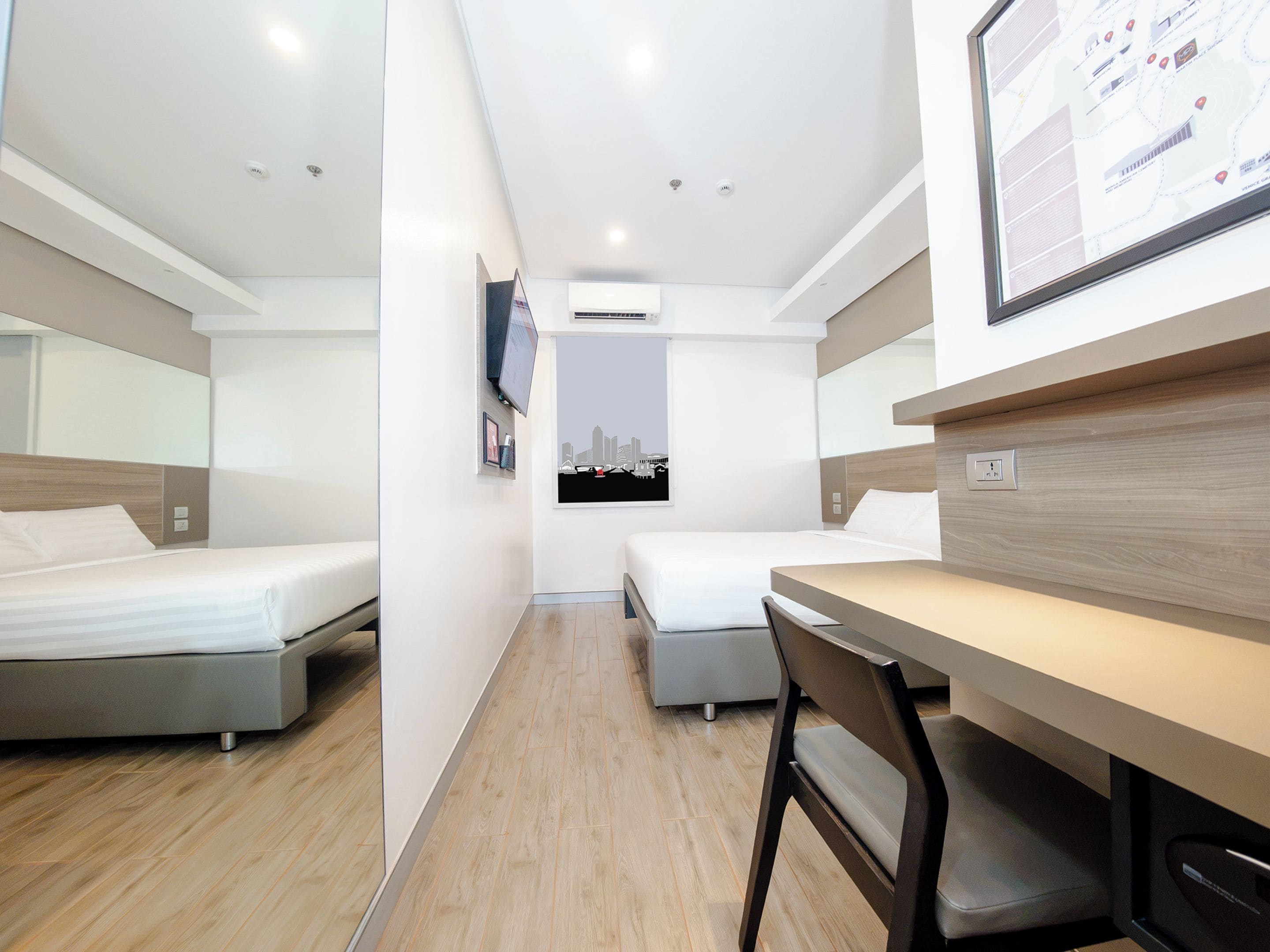 A modern hotel room with two beds, a desk, and a chair.