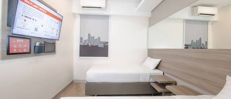 A modern hotel room with a bed, a desk, a mounted TV, and an air conditioning unit.