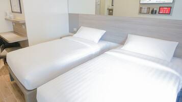 A hotel room with two single beds, a bedside table, a chair, a small desk, a mirror, and a wall-mounted information board.