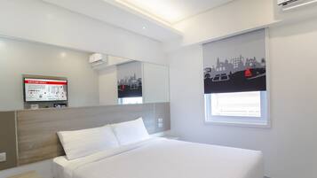 A modern hotel room with a large bed, a mounted TV, a window with a cityscape view, and a built-in desk.