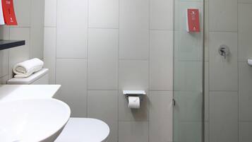 Ett modernt badrum med en dusch som är avskärmad med glasväggar, ett vitt handfat och en toalett.