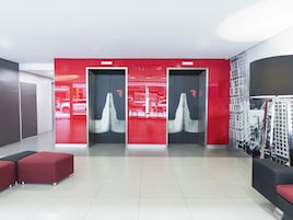A modern lobby with two elevators, red seating area, and a cityscape mural on the wall.
