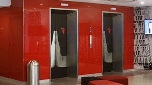 A modern elevator area with red walls, two elevators, a trash bin, and a seating area. - Red Planet Cubao Aurora Boulevard (Quezon City)