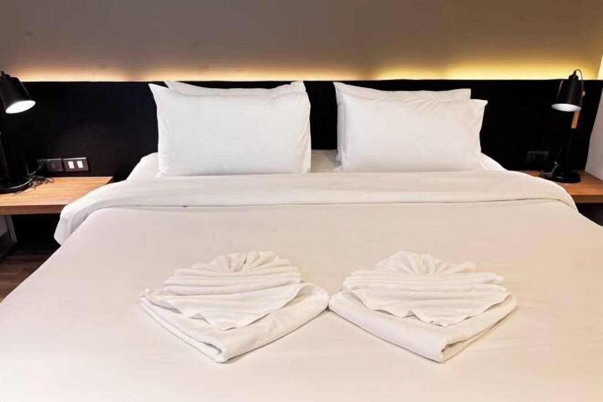 A neatly made bed with white linens and towels arranged in a heart shape on the bed.