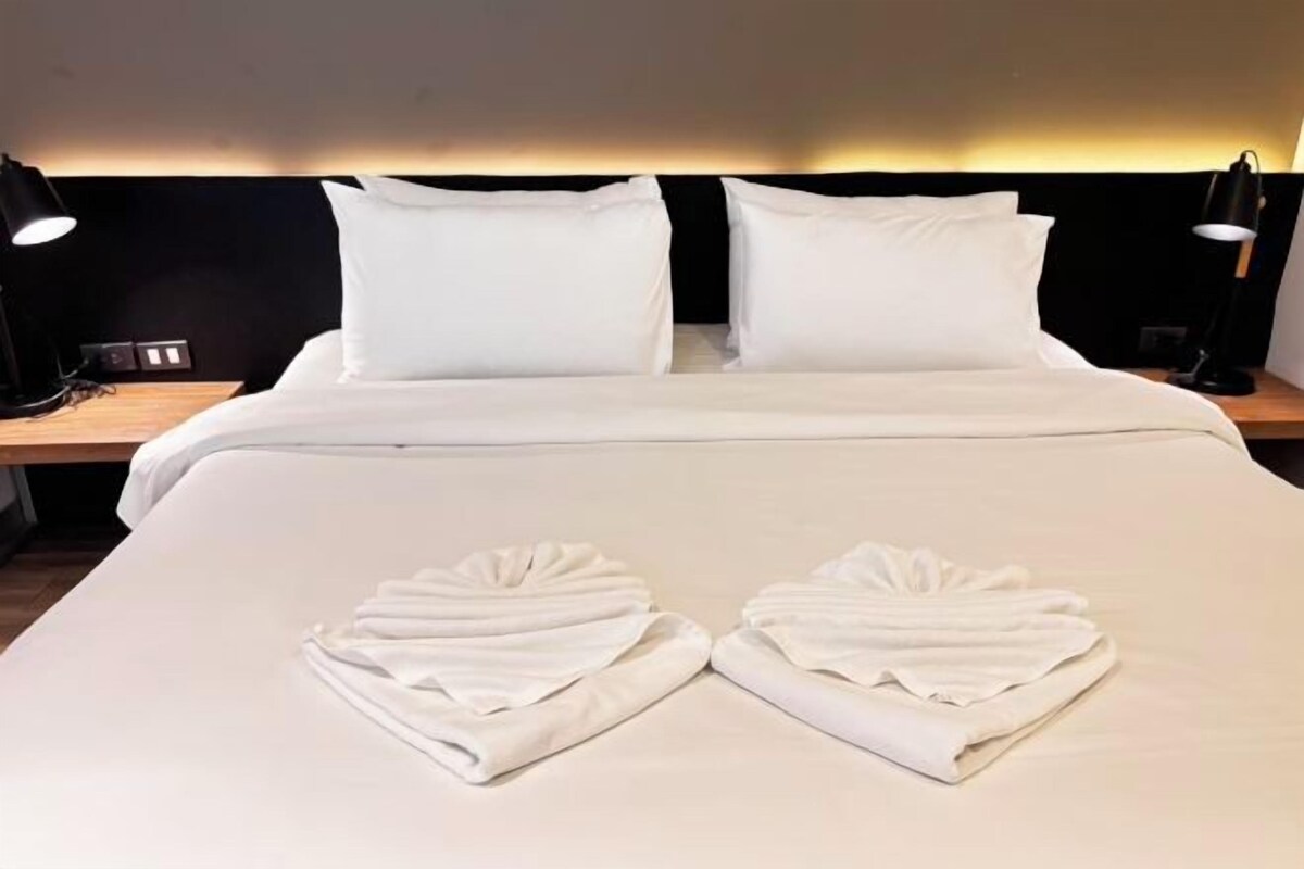 A neatly made bed with white linens and towels arranged in a heart shape on the bed.