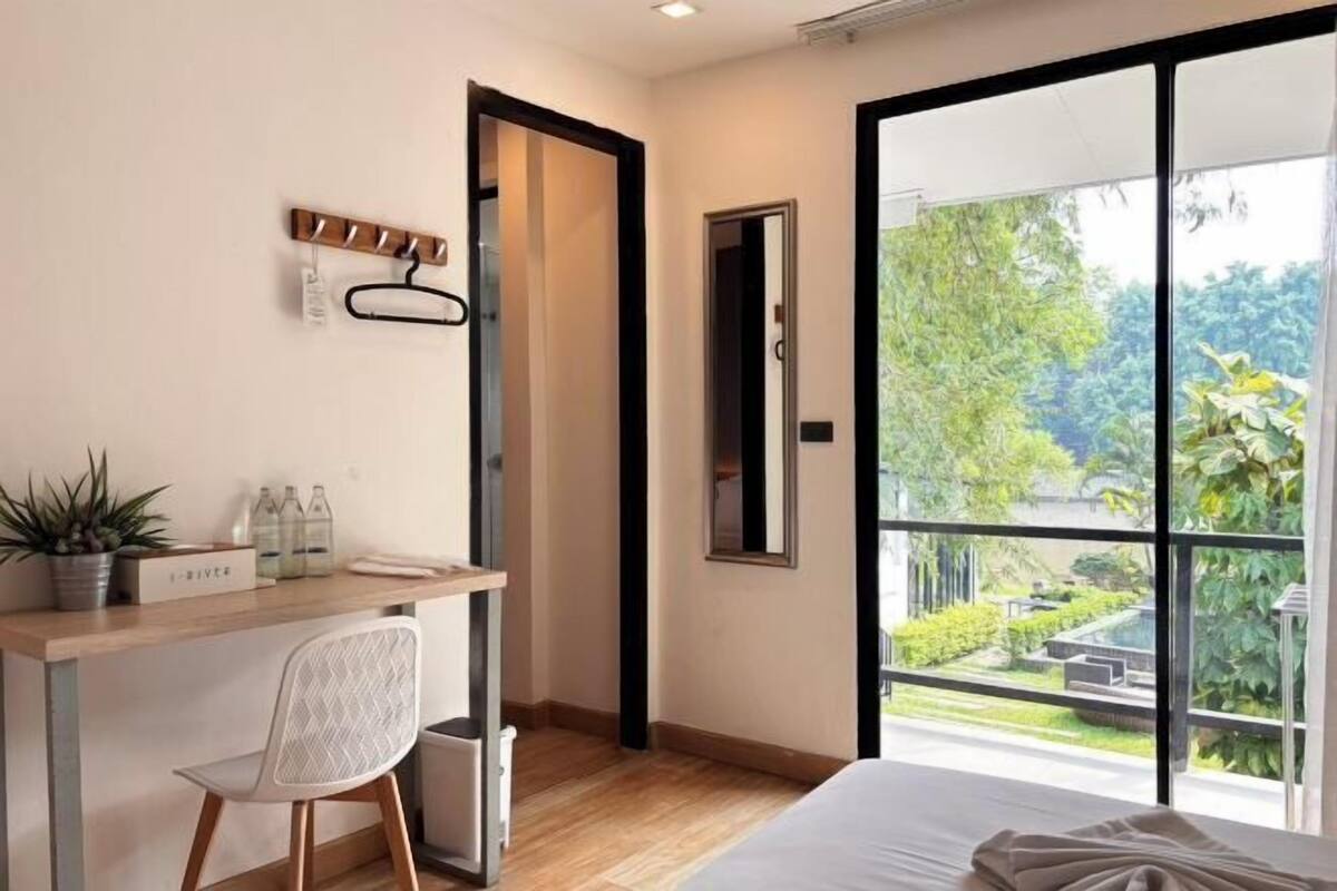 A modern hotel room with a large window, a desk with a chair, a bed, and a small trash bin.
