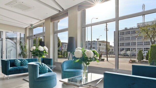 Eine moderne Hotelhalle mit großen Fenstern, blauem Mobiliar und einem Glastisch.