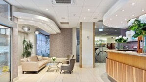 Eine moderne Hotelhalle mit Empfangstresen, Sitzgelegenheiten und einer großen Pflanze.