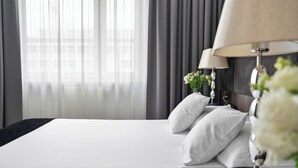 Ein Hotelzimmer mit einem großen Bett, zwei Nachttischen mit Lampen und einem Fenster mit durchsichtigen Vorhängen.