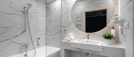 Une salle de bain moderne avec un mur en marbre, un miroir rond, une baignoire, un lavabo et un porte-serviettes.