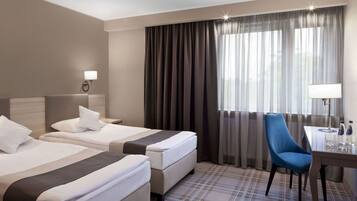 A hotel room with two beds, a desk, a chair, and a large window with curtains.