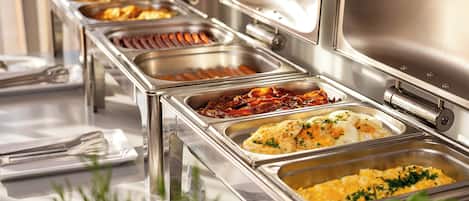 A buffet with various food items in stainless steel containers, including what appears to be eggs, bacon, and other breakfast items.