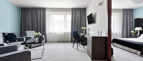 A modern hotel room with a grey sofa, a small desk, a bed, and a large mirror.