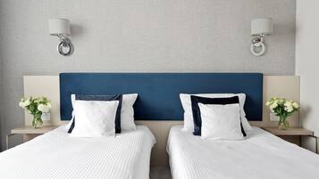 Habitación de hotel con dos camas, cabecero azul, ropa de cama blanca y dos mesitas de noche con lámparas y jarrones.