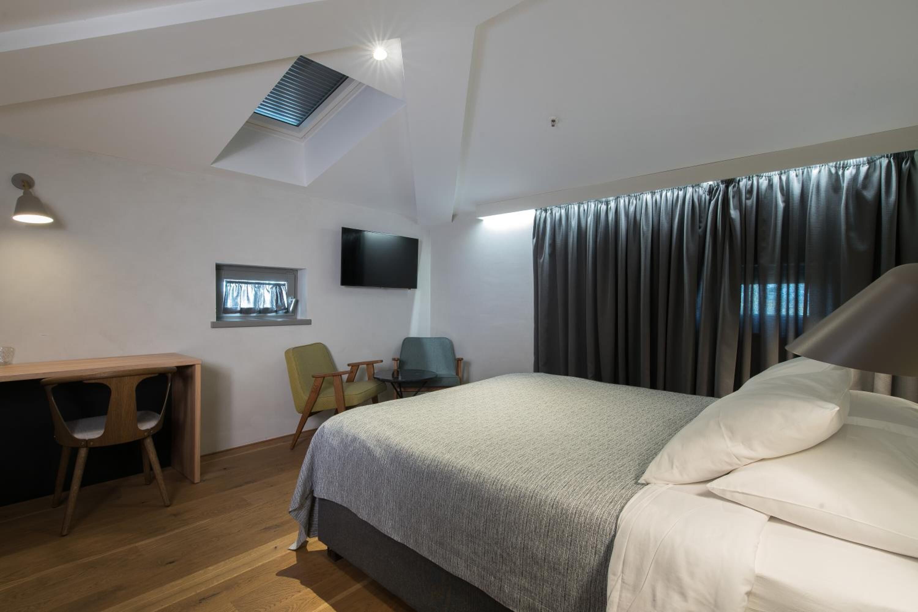 Ein Hotelzimmer mit Bett, Schreibtisch, zwei Stühlen, einem Flachbildfernseher und einem Fenster mit Vorhängen.
