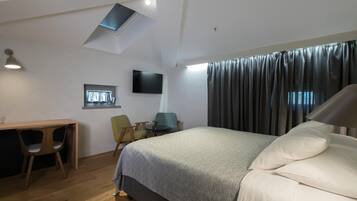 Ein Hotelzimmer mit Bett, Schreibtisch, zwei Stühlen, einem Flachbildfernseher und einem Fenster mit Vorhängen.