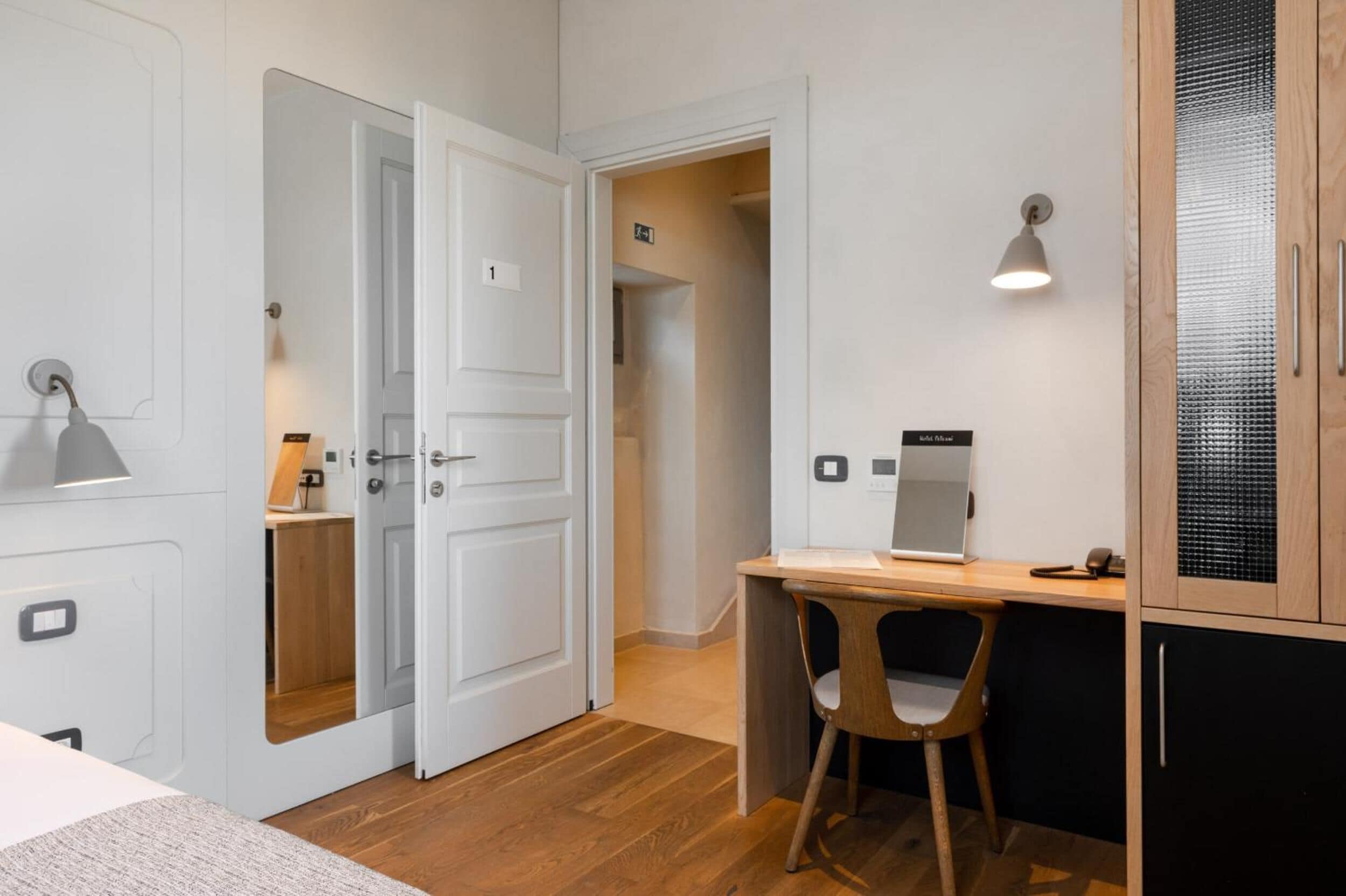 A hotel room with a wooden desk, a chair, a bed, and a wardrobe.
