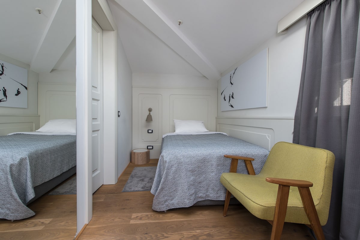 Ein Schlafzimmer mit zwei Betten, einem Sessel, einem Nachttisch und einem kleinen Hocker.