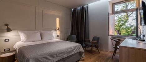 Ein modernes Hotelzimmer mit einem großen Bett, einem Schreibtisch, einem Stuhl und einem Fenster mit Blick auf Bäume.