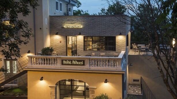 Hotel con restaurante en la planta baja, fachada de ladrillo, balcón con mesas al aire libre y un cartel con el nombre del hotel.