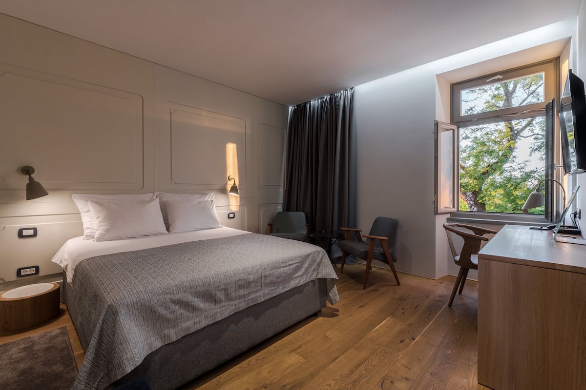 Ein Schlafzimmer mit Bett, Nachttisch, Lampe, Stuhl, Schreibtisch und Fenster.