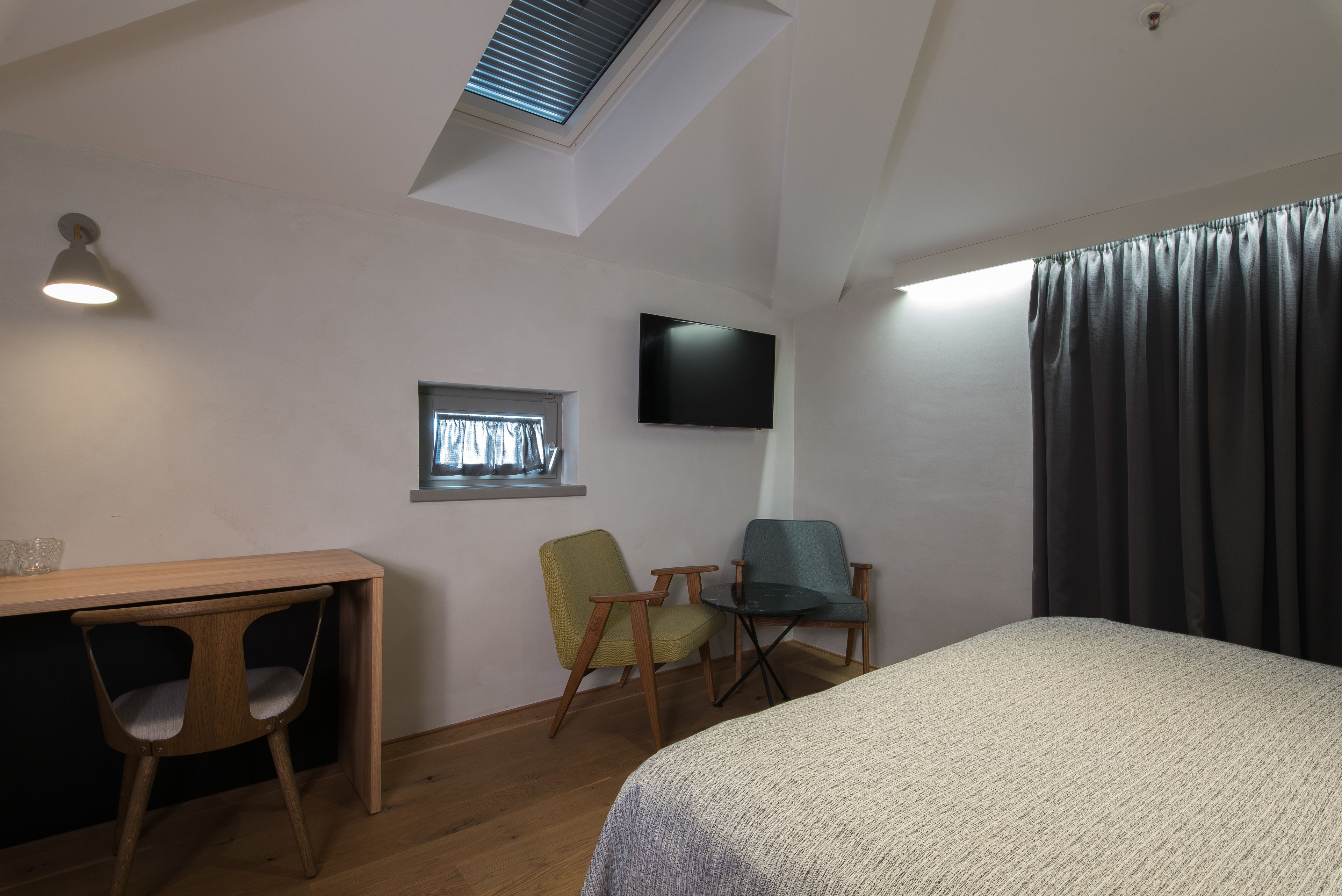 A room with a bed, a desk, two chairs, a TV, a window, and a skylight.