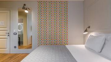 A hotel room with a bed, a mirror, a door, and a wall with a polka dot pattern.