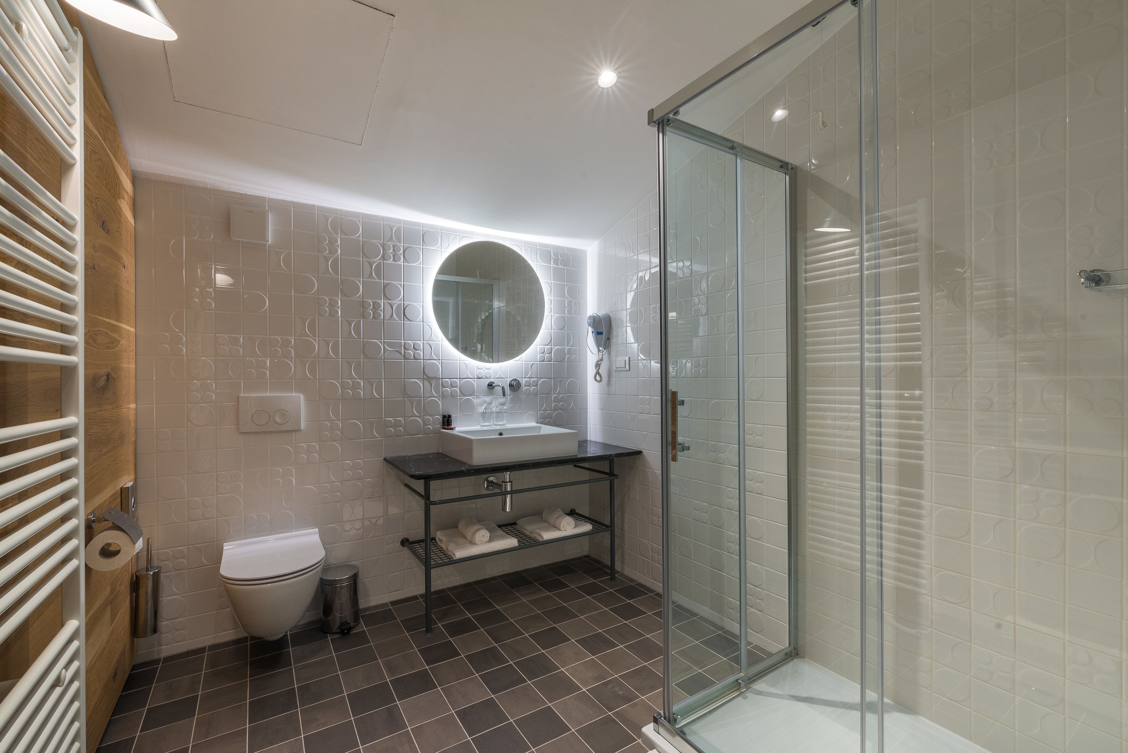 Un bagno moderno con cabina doccia in vetro, lavandino bianco e specchio rotondo.