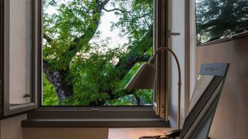 Une pièce avec une grande fenêtre, un bureau, une lampe et un tableau encadré.