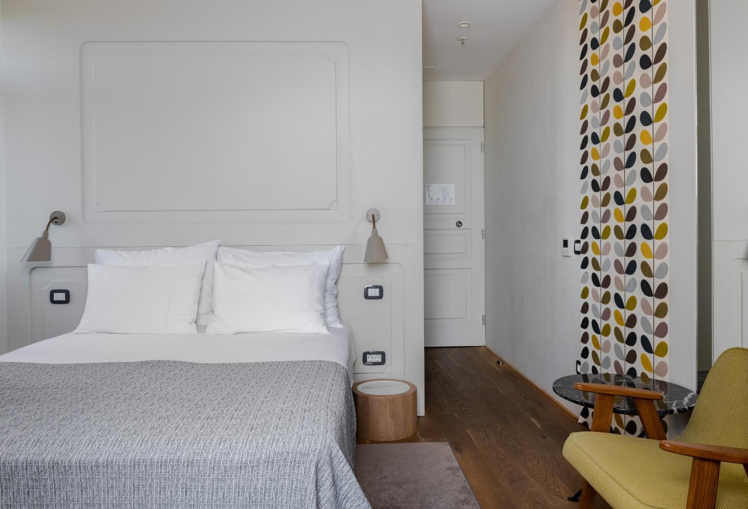 Un dormitorio moderno con cama, mesitas de noche, una silla y una pared con diseño de hojas.