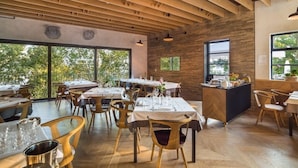 Un restaurante con vigas de madera en el techo, ventanas amplias y una zona de bar central.