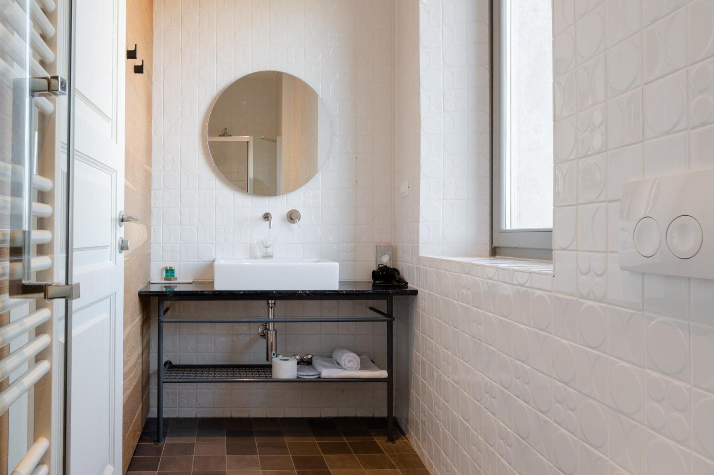 A bathroom with a white sink, a round mirror, and a window.