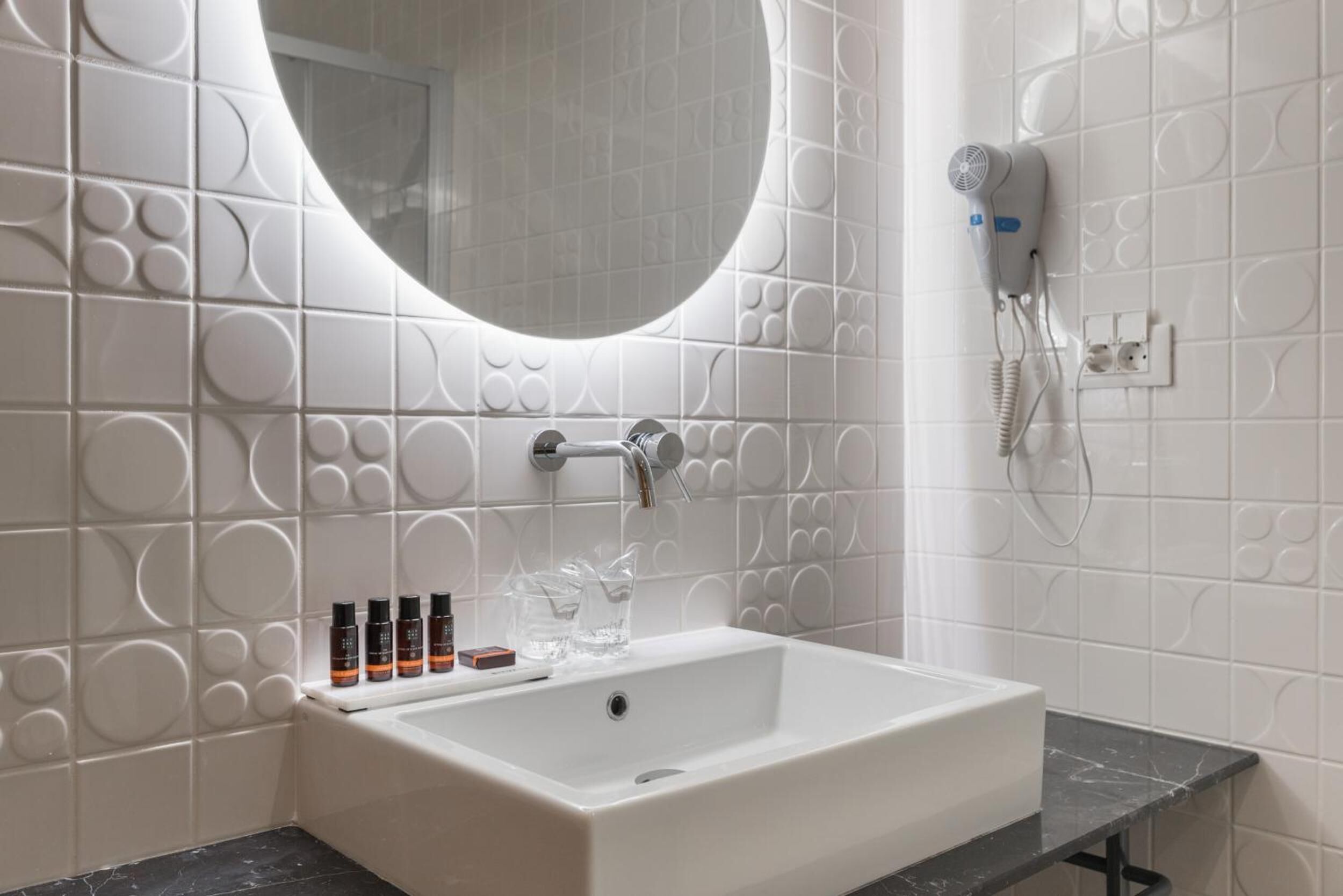 Een badkamer met een wit wastafelmeubel, een spiegel en een haardroger aan de muur.