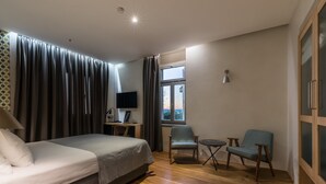 Habitación de hotel con cama, escritorio con computadora, dos sillas, ventana con cortinas y televisor en la pared.