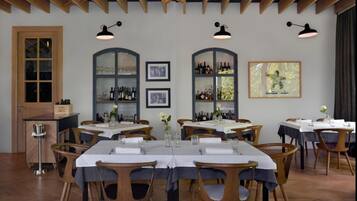 A dining area with wooden tables, chairs, and a bar area with shelves of bottles.