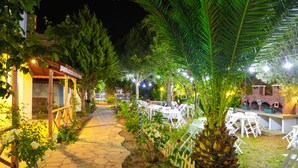 A nighttime outdoor patio area with stone pathways, white outdoor furniture, and string lights. - Destina Suit Hotel (Bozcaada)