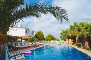 A swimming pool with lounge chairs and a building with a red roof in the background. - Destina Suit Hotel (Bozcaada)