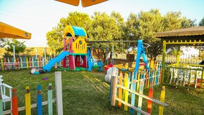 A playground with a slide, climbing structures, and a fenced area. - Destina Suit Hotel (Bozcaada)