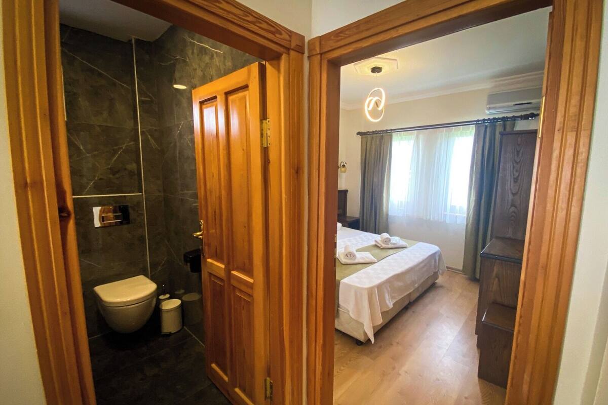 A hotel room with a bathroom, a bed, and a wooden wardrobe.