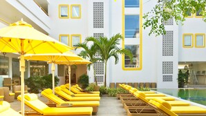 A poolside area with yellow sun loungers and umbrellas, surrounded by potted plants and a building with decorative windows. - Bloom Hotel – Calangute (Calangute)