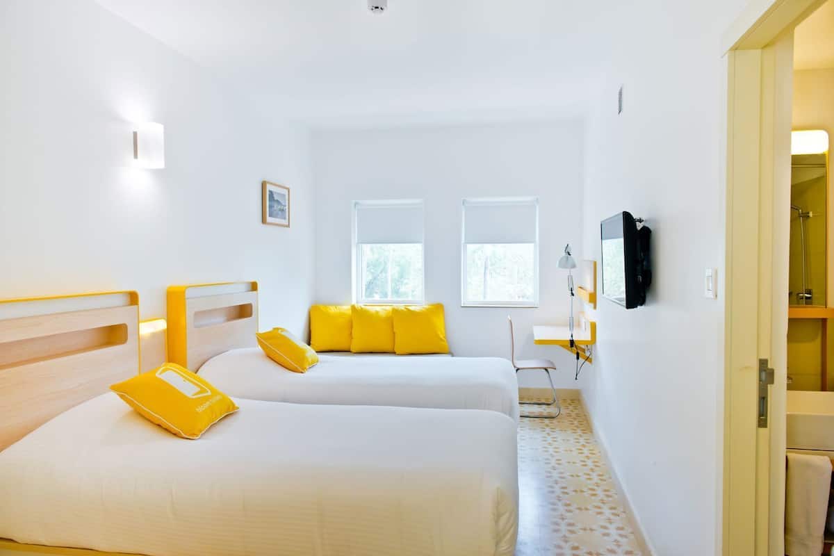 A hotel room with two beds, a desk, a chair, a TV, and a window.