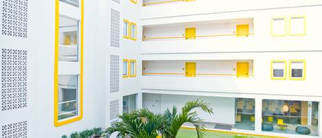 A multi-story hotel with balconies, a pool, and potted plants.