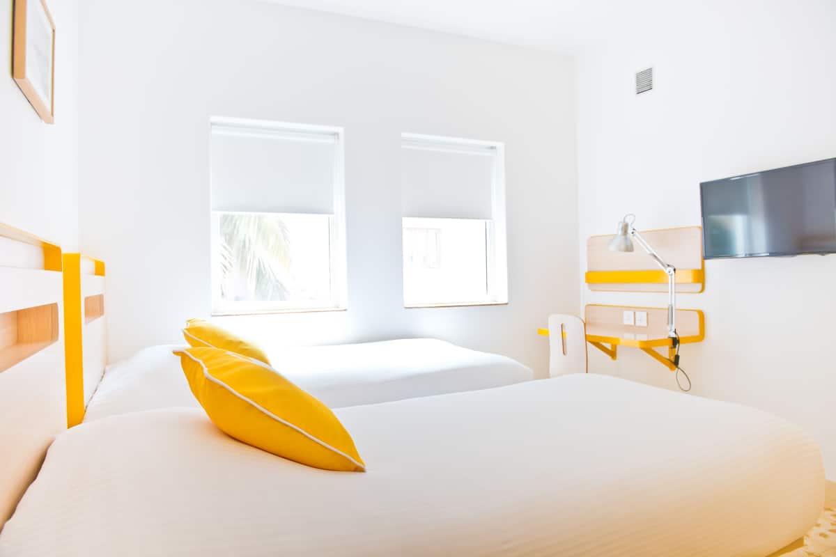 A hotel room with two beds, a television, and a window with a view of palm trees.